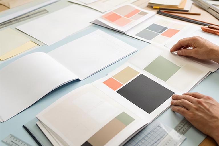 Aufgeschlagene Broschüren und InDesign-Layouts auf einem Arbeitstisch im Kursraum